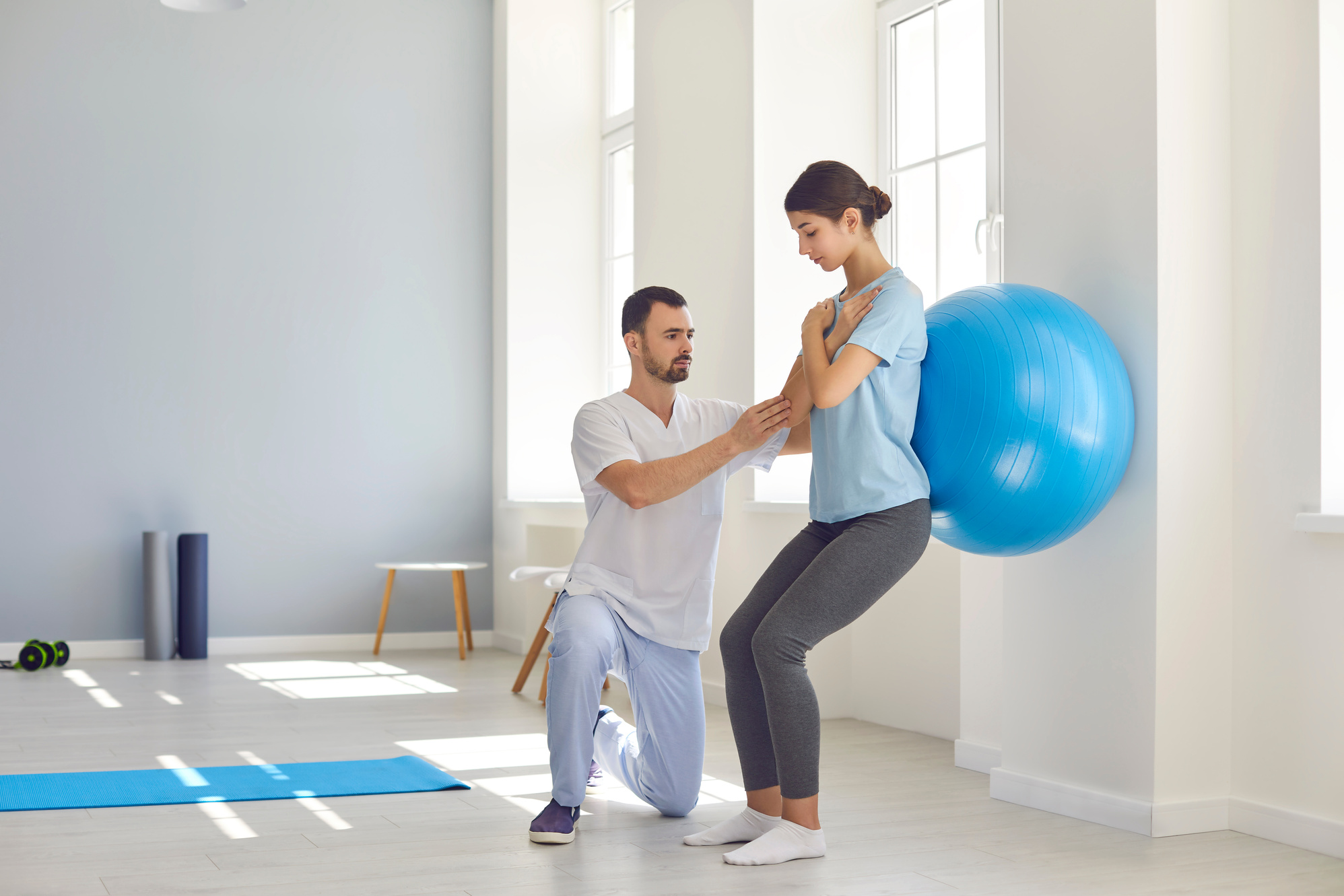 Physiotherapist Helping Young Woman Recover from Back Injury Using Big Soft Ball